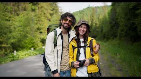 A-guy-and-a-girl-tourists-in-special-clothes-for-hiking-pose-with-a-camera-against-the-backdrop-of-a-mountain-forest