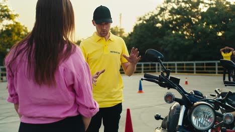 A-driving-instructor-in-a-yellow-t-shirt-tells-a-female-student-in-a-pink-t-shirt-how-to-behave-while-driving-a-motorcycle