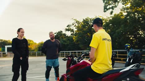 Driving-instructor-in-a-yellow-T-shirt-tells-a-guy-and-a-girl-how-to-sit-on-a-motorcycle.-Driving-practice-after-studying-theory