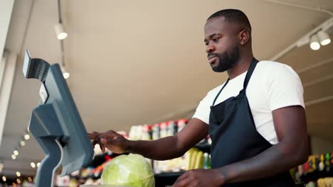 Close-up-shot-of-a-Black-skinned-man-in-a-white-t-shirt-and-black-apron-weighing-vegetables-on-an-electronic-scale-in-a-supermarket
