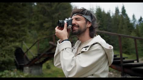 Portrait-of-a-tourist-brunette-guy-who-photographs-a-view-of-the-green-forest.-Guy-in-a-white-jacket-on-a-hike