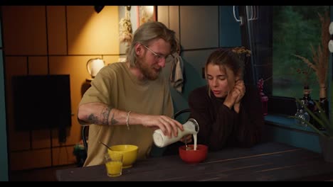 a-blond-guy-in-glasses-with-a-beard-prepares-a-morning-breakfast-of-milk-and-cereal-for-his-blond-girlfriend-in-a-cozy-room