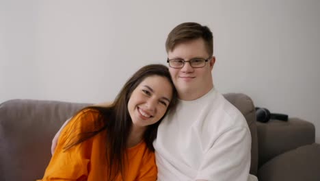 Young-man-with-Down-syndrome-with-his-female-friend-embracing-sit-on-sofa