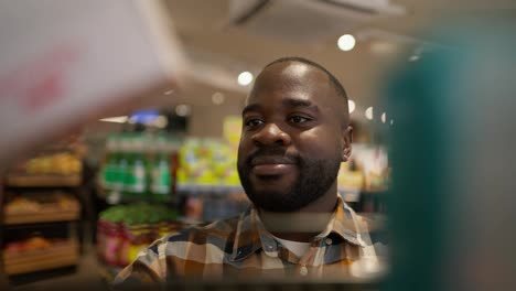 Nahaufnahme-Eines-Schwarzen-Mannes,-Der-In-Einem-Supermarkt-Eines-Von-Zwei-Produkten-Auf-Dem-Boden-Auswählt