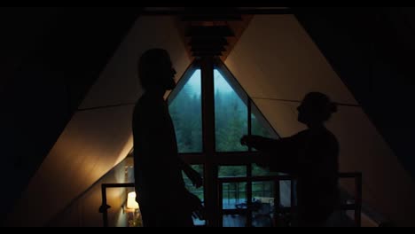 Silhouettes-of-a-guy-and-a-girl-are-hugging-against-the-background-of-a-window-overlooking-a-green-mountain-forest-in-a-dark-room.-romantic-meeting