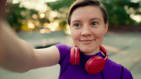 First-person-view:-A-girl-with-a-short-haircut-in-a-purple-top-in-red-headphones-takes-a-selfie-in-a-skate-park-in-summer