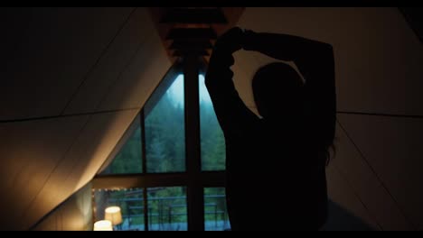 Silhouette-of-a-girl-who-looks-out-the-window-at-the-green-forest-in-the-mountains-and-stretches.-Video-filmed-in-high-quality