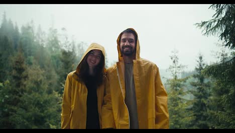 Happy-couple:-a-guy-and-a-girl-in-yellow-jackets-stand-against-the-backdrop-of-a-foggy-mountain-forest-and-smile