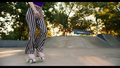 Close-up-shot:-A-young-girl-with-a-short-haircut-in-a-purple-top-and-striped-pants-roller-skates-in-a-skate-park-on-a-concrete-surface.-Outdoor-activities-in-summer