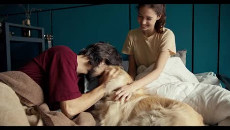 A-brunette-and-a-brunette-are-stroking-a-dog-in-bed-against-a-turquoise-wall.-Hanging-out-with-your-pets-at-home