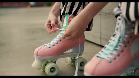 Close-up:-a-character-in-striped-pants-sits-on-a-bench-and-laces-up-his-pink-skates.-Preparing-for-roller-skating-in-the-skate-park-in-summer