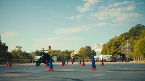 Two-driving-instructors-in-yellow-t-shirts-hone-their-skills-in-motorcycle-maneuverability.-Two-guys-go-around-obstacles-on-a-motorcycle