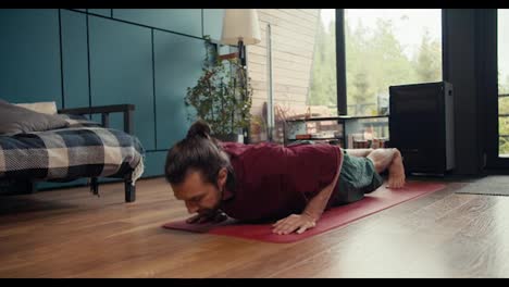 A-brunette-guy-in-a-red-T-shirt-does-push-ups-on-a-special-rug-in-a-country-house-overlooking-a-green-forest