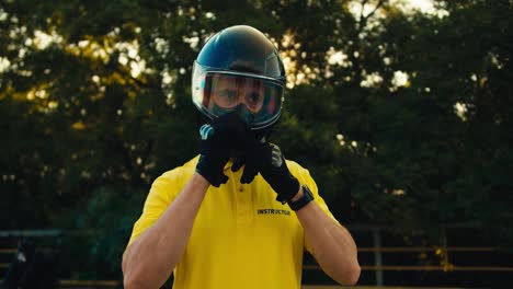 Portrait-of-a-motorcycle-driving-instructor-in-a-yellow-T-shirt-who-takes-off-the-protection-from-a-motorcycle-helmet-and-looks-to-the-side