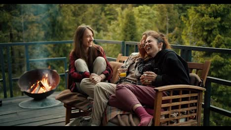 Three-girls-are-chatting-and-laughing-while-sitting-on-a-sofa-near-the-barbecue-in-a-country-house-overlooking-the-forest-and-mountains