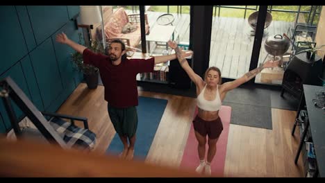 Overview-and-top-view:-a-blonde-girl-and-a-brunette-guy-are-doing-yoga-on-special-mats-in-red-and-blue-in-a-country-house