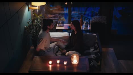 Romantic-evening:-a-guy-and-a-girl-are-sitting-on-a-devan-in-a-room-lit-by-candles.-The-guy-proposes-to-the-girl,-she-agrees-and-they-hug