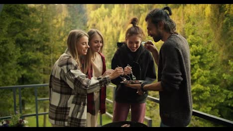 A-group-of-friends-try-the-food-they-cooked-on-the-grill-in-a-country-house-overlooking-the-mountains-with-a-coniferous-forest.-The-guy-holds-a-plate-of-food-and-stands-near-the-barbecue