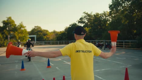 A-driving-instructor-in-a-yellow-T-shirt-indicates-to-a-motorcyclist-which-way-he-should-turn-with-the-help-of-orange-cones