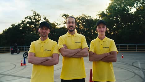 A-team-of-driving-instructors-in-a-yellow-T-shirt-put-their-hands-on-their-chests-and-pose.-Trio-of-driving-instructors-in-a-driving-school