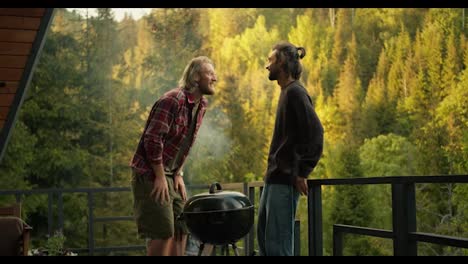 Two-friends-emotionally-communicate-and-laugh-at-a-picnic-overlooking-a-coniferous-forest.-Communication-while-cooking-on-the-grill