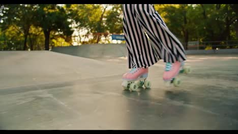 Close-up-shot-of-a-person-in-striped-pants-and-pink-roller-skates-riding-on-a-concrete-floor-in-a-skate-park-in-summer