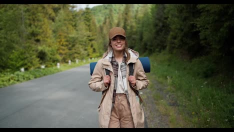 A-blonde-girl-in-special-clothes-for-a-hiker-of-light-brown-color-poses-near-the-road-being-in-a-mountain-forest