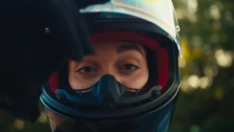 Close-up-shot-of-a-girl-opening-the-protection-of-a-motorcyclist's-helmet-and-looking-at-the-camera