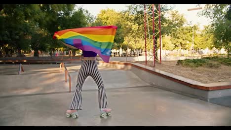 A-happy-girl-with-a-short-haircut-in-a-purple-tank-top-and-striped-pants-rides-pink-roller-skates-in-a-skate-park-and-wraps-herself-in-the-LGBT-flag