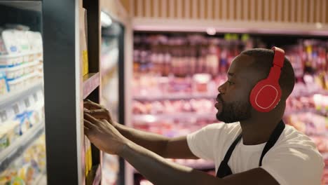 Close-up-shot-of-a-Black-skinned-man-in-red-headphones-and-a-black-apron-adjusting-goods-on-the-shelves-in-a-supermarket