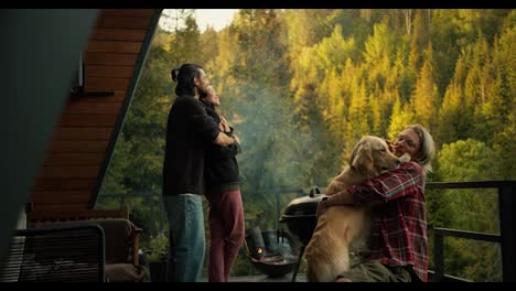 A-group-of-friends-on-a-picnic-overlooking-the-mountains-and-coniferous-forest.-A-brunette-guy-is-hugging-a-brunette-girl,-and-a-blond-man-is-stroking-a-large-light-colored-dog
