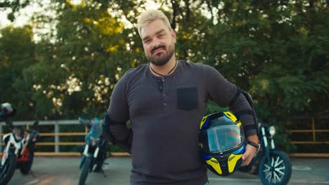A-biker-with-white-hair-with-a-beard-and-an-earring-stands-and-holds-a-motorcycle-helmet-in-his-hand
