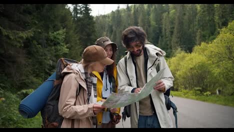 A-trio-of-tourists-get-lost-and-are-looking-at-a-map-to-figure-out-where-to-go-next.-People-in-hiking-clothes-sort-out-where-to-have-next-in-mountainous-terrain