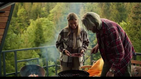 The-couple-is-relaxing-and-having-a-picnic-in-a-country-house-overlooking-the-forest-and-mountains.-The-guy-and-the-blonde-girl-spend-time-together-at-the-barbecue-at-a-picnic