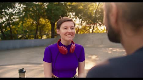 A-brunette-guy-in-a-gray-t-shirt-communicates-with-a-girl-with-a-short-haircut-in-a-purple-top-and-red-headphones-in-a-skate-park-in-summer