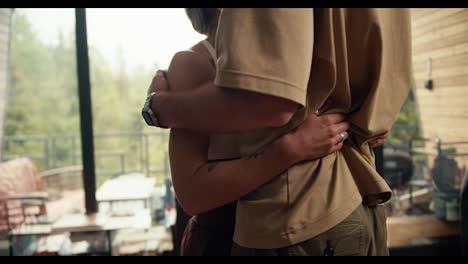 Close-up-shot:-a-guy-and-a-girl-hugging-in-an-industrial-country-house-overlooking-a-green-coniferous-forest