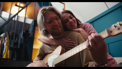 A-guy-a-girl-spends-time-together-a-blond-guy-with-a-beard-in-glasses-plays-the-electric-guitar-a-brunette-girl-hugged-him-and-listens