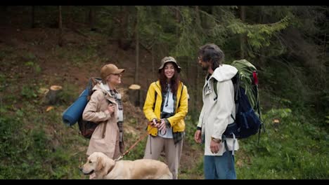 A-trio-of-hikers-in-special-hiking-clothes-with-large-backpacks,-together-with-their-light-colored-dog,-communicate-in-the-middle-of-the-forest