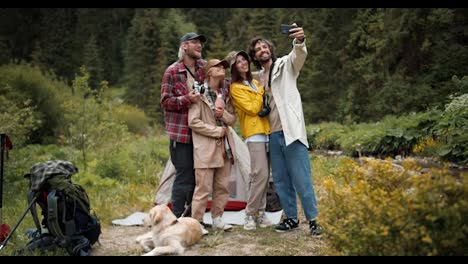 A-group-of-happy-tourists-in-special-hiking-clothes-take-a-selfie-against-the-backdrop-of-a-green-forest.-Active-lifestyle,-walking-and-hiking.-Selfie-as-a-memory-of-the-event