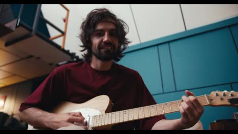 A-man-with-shaggy-hair-with-a-beard-in-a-red-T-shirt-plays-the-electric-guitar-and-looks-at-the-camera