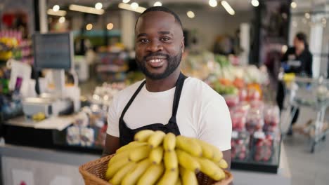 Portrait-of-a-black-skinned-man-in-a-brown-t-shirt-and-black-apron-posing-with-yellow-bananas-in-his-hands-in-a-supermarket