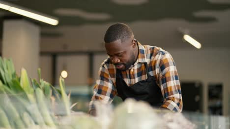 Portrait-of-a-Black-skinned-man-in-a-plaid-shirt-and-black-apron-sorting-vegetables-on-a-supermarket-counter