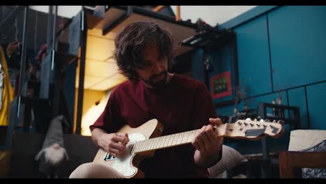 A-brunette-guy-with-patlaty-hair-in-a-red-T-shirt-plays-the-electric-guitar-at-home.-Video-filmed-in-high-quality