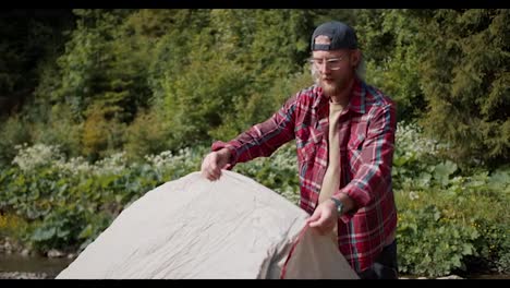 Shooting-near-a-blond-man-with-a-beard-in-glasses-in-a-red-plaid-shirt-lays-out-and-sets-up-a-tent-against-the-backdrop-of-the-forest