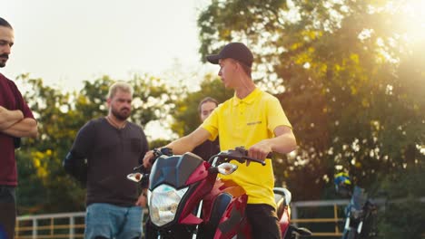 A-driving-instructor-in-a-yellow-T-shirt-tells-his-students-how-to-sit-on-a-motorcycle-and-how-to-drive-it-correctly.-Teachings-at-the-site-of-a-motorcycle-school-in-sunny-weather