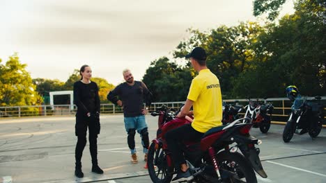 Happy-students-in-moto-school-chatting-with-moped-driving-instructor.-A-man-in-a-yellow-T-shirt-communicates-with-a-man-with-a-beard-and-a-girl
