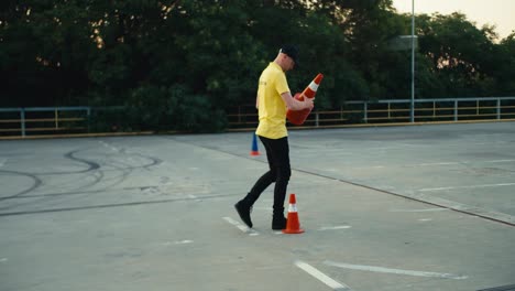 A-man-in-a-yellow-T-shirt-lays-out-orange-cones-on-the-road.-Motorcycle-driver-laying-out-orange-cones-for-student-training