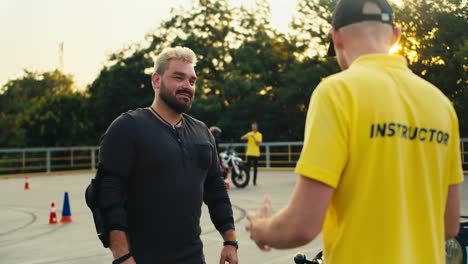 A-male-biker-in-protective-gear-with-a-thick-beard-communicates-with-a-driving-instructor-in-a-yellow-T-shirt