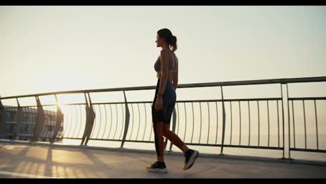 A-young-athletic-girl-in-sportswear-walks-along-the-bridge-in-the-city-in-the-morning.-Sunrise-and-morning-run