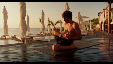 Yogi-Typ-Nimmt-Morgens-An-Einem-Sonnigen-Strand-Eine-Besondere-Pose-Zum-Dehnen-Und-Meditieren-Ein.-Der-Typ-Sitzt-Auf-Dem-Boden-Der-Bretter-Auf-Einem-Speziellen-Teppich